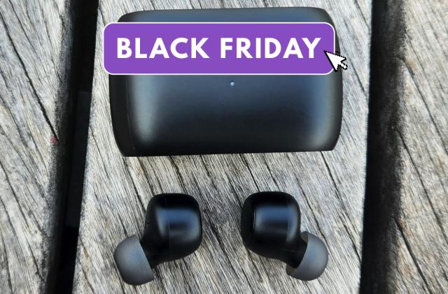 Earbuds with the black friday logo on top sit on a wooden table. 