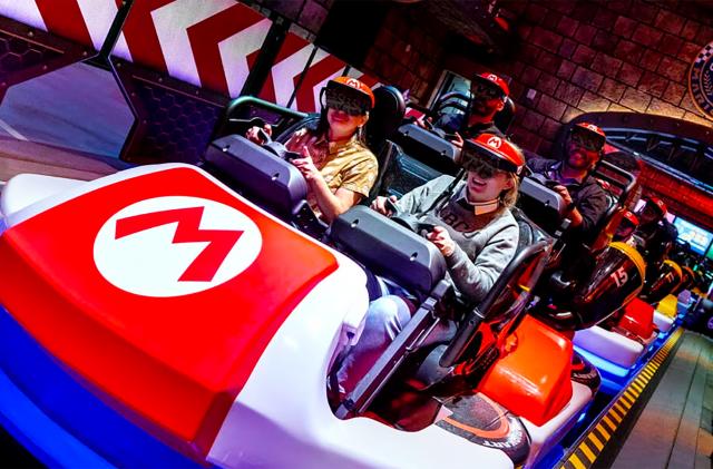 Smiling park visitors sit inside cars at the Universal Studios ‘Mario Kart’ ride. The car has a Mario ‘M’ logo on it.