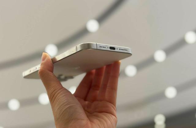 The iPhone 15 Pro Max held up against a ceiling of lights, showing its USB-C port.  