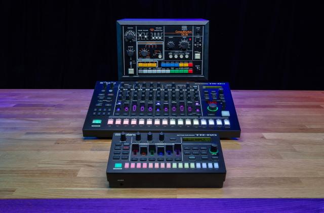 The Roland TR-8S, TR-6S and CR-78 are lined up front-to-back on a wooden table with a black background.