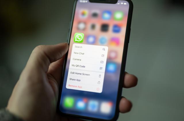A hand holding an iPhone displaying WhatsApp.