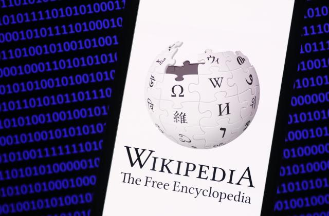 Wikipedia logo displayed on a phone screen and a binary code displayed on a screen are seen in this illustration photo taken in Krakow, Poland on January 19, 2023. (Photo by Jakub Porzycki/NurPhoto via Getty Images)
