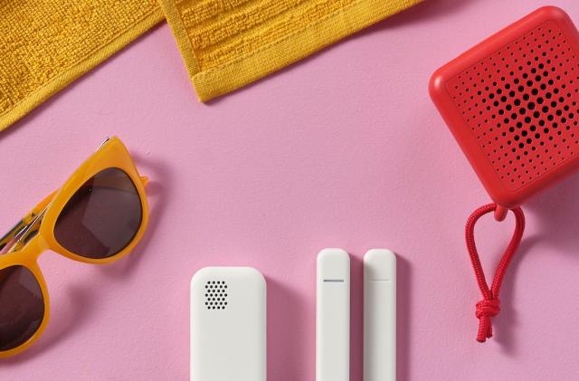 Three white sensors lay on a pink background next to yellow sunglasses. 