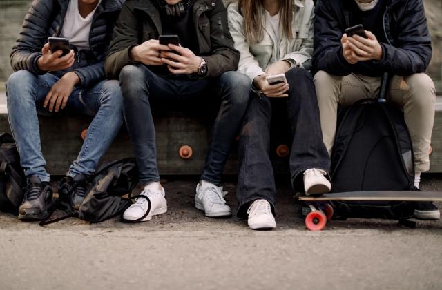 Low section of teenage boys and girl using smart phone while sitting at park
