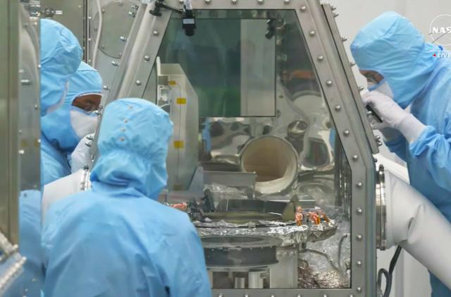Several scientists peer into a sealed glass module where the asteroid Bennu samples stored.