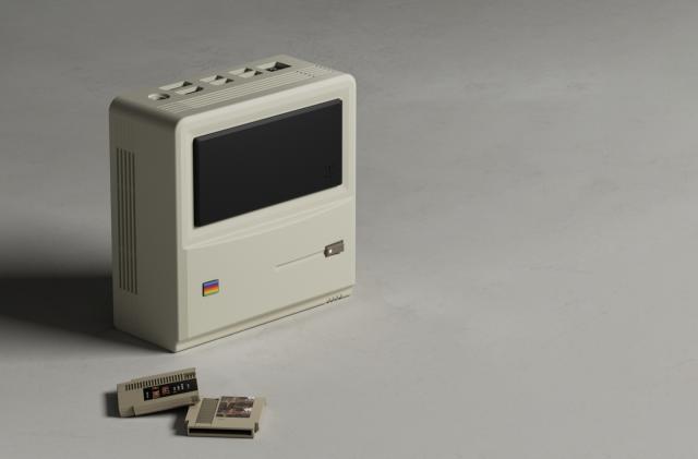 Ayaneo's AM01 mini PC with two game cartridges sitting in front. The mini PC looks like Apple's original Macintosh.