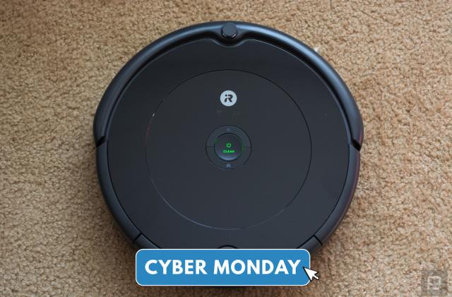 A Roomba robot vacuum sits on a carpet under a Cyber Monday logo. 